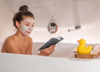 Bath at home woman relaxing taking a warm bath reading book cozy enjoying free time putting facial clay mask pampering weekend. Bubble bath spa time