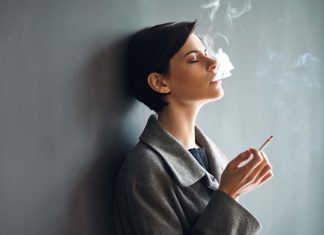 Portrait of fashionable woman smoking a cigarette on dark backgr
